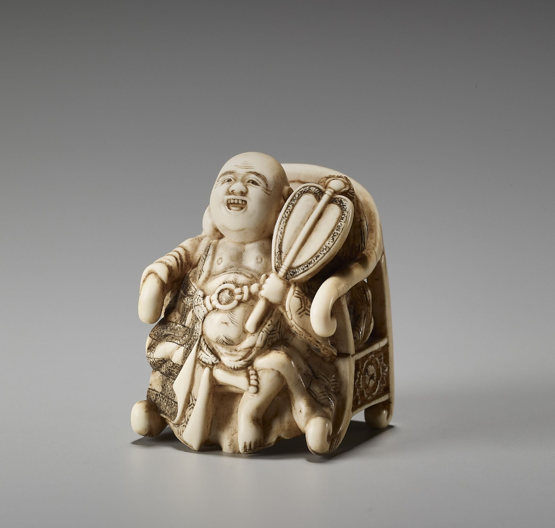 AN UNUSUAL IVORY NETSUKE OF HOTEI ON A THRONE BY CHIKUSAI