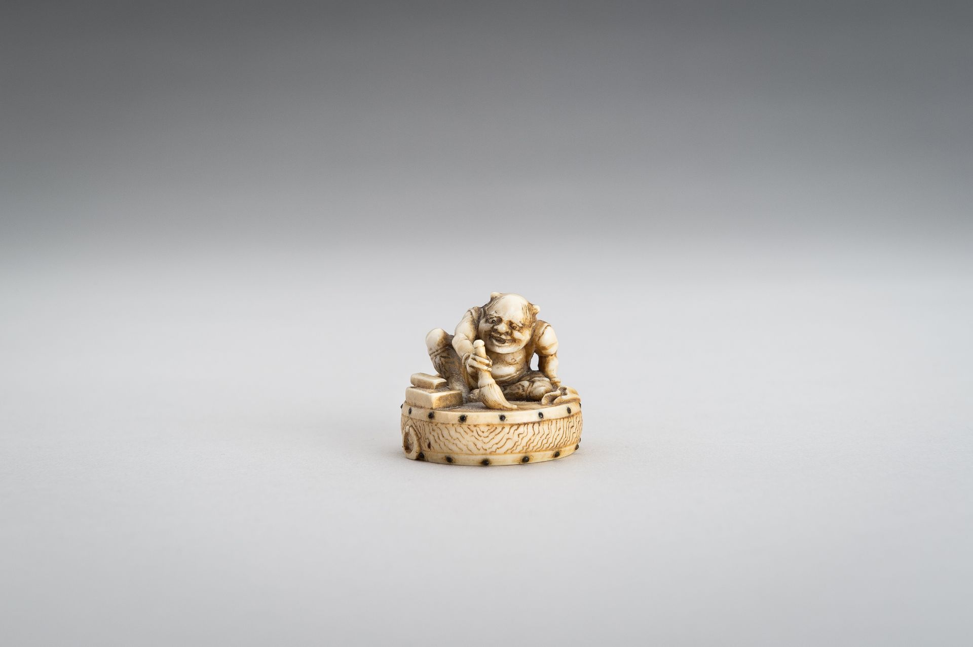 GYOKUSHU: AN IVORY NETSUKE OF AN ONI CLEANING A DRUM - Image 2 of 12