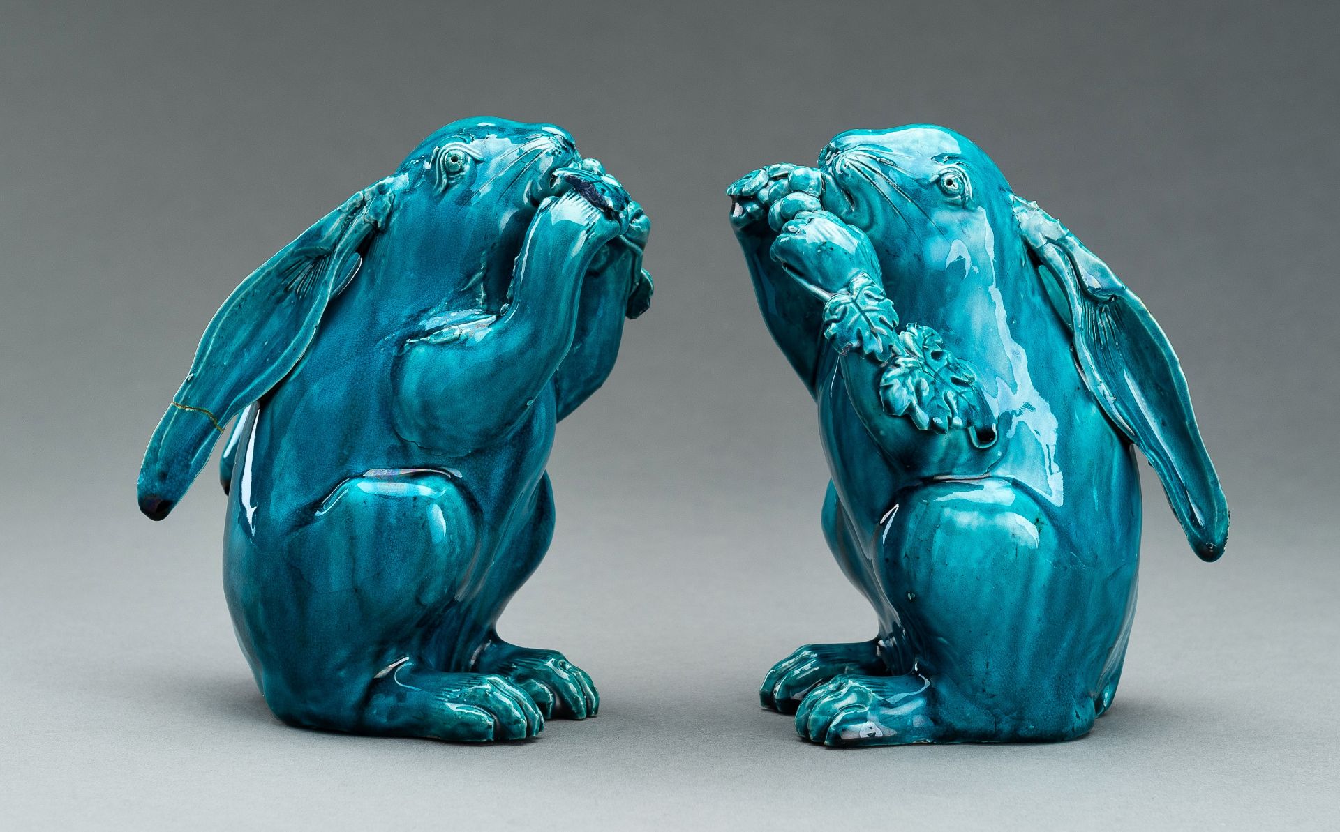 A PAIR OF TURQUOISE GLAZED CERAMIC FIGURES OF RABBITS EATING BERRIES