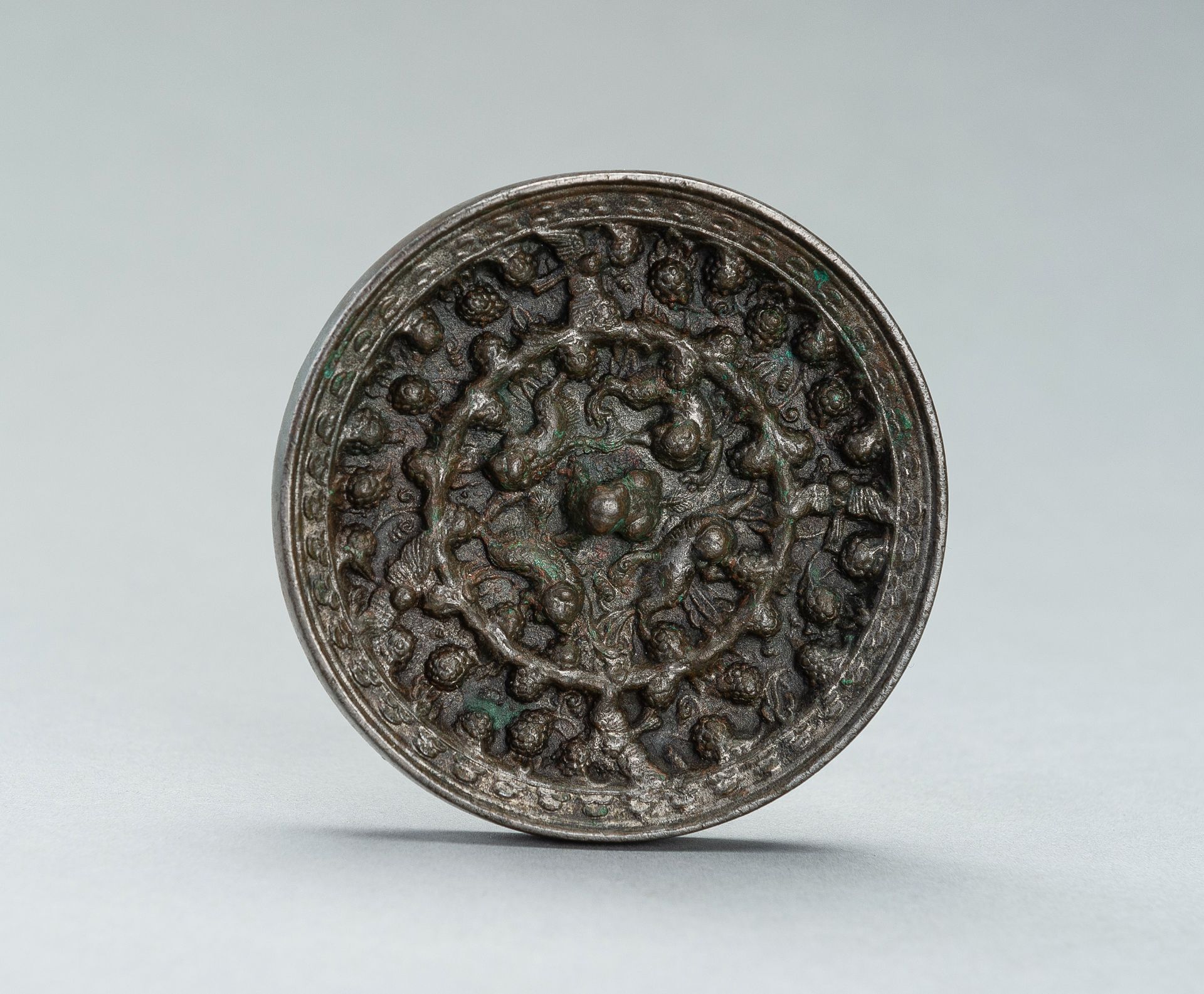 A SILVERY TANG DYNASTY BRONZE 'LION AND GRAPEVINE' MIRROR