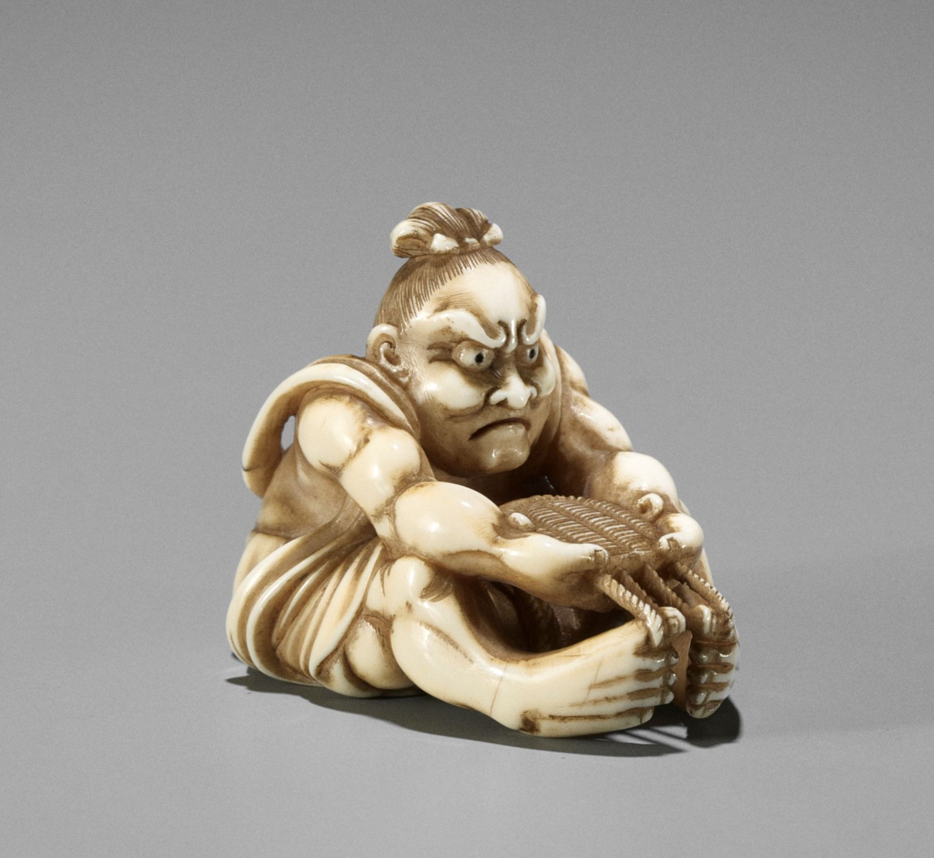 A FINE IVORY NETSUKE OF NIO WEAVING A SANDAL