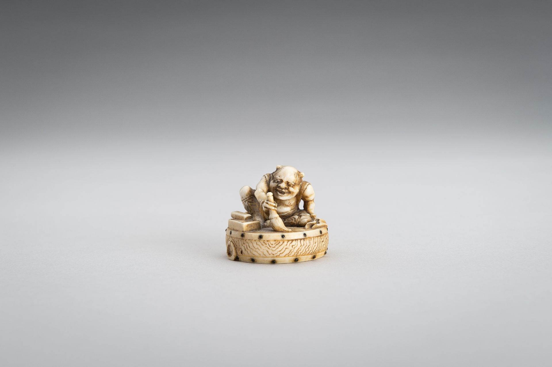 GYOKUSHU: AN IVORY NETSUKE OF AN ONI CLEANING A DRUM - Image 4 of 12