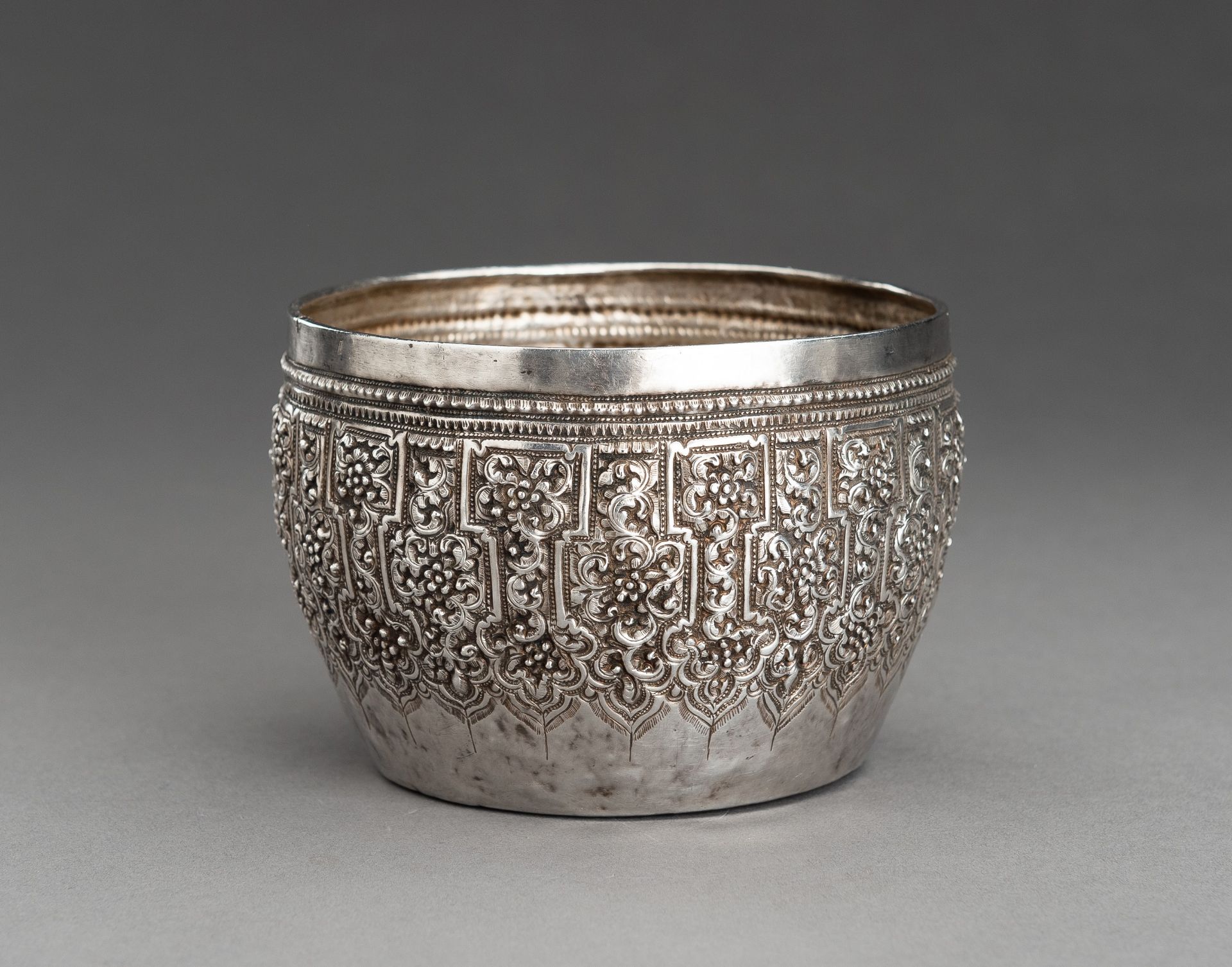 AN EMBOSSED BURMESE SILVER BOWL WITH FLORAL RELIEF