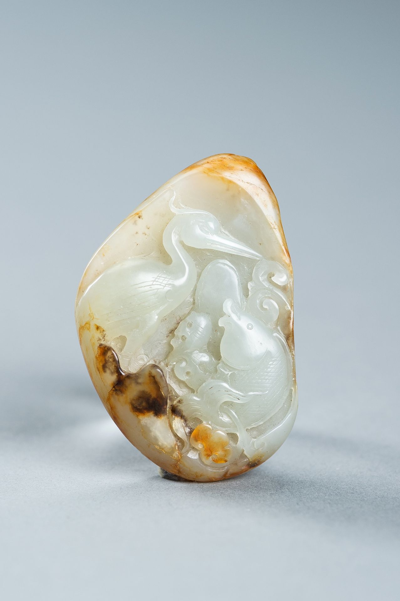 A CELADON AND RUSSET JADE 'FISH AND CRANE' PENDANT, c. 1920s