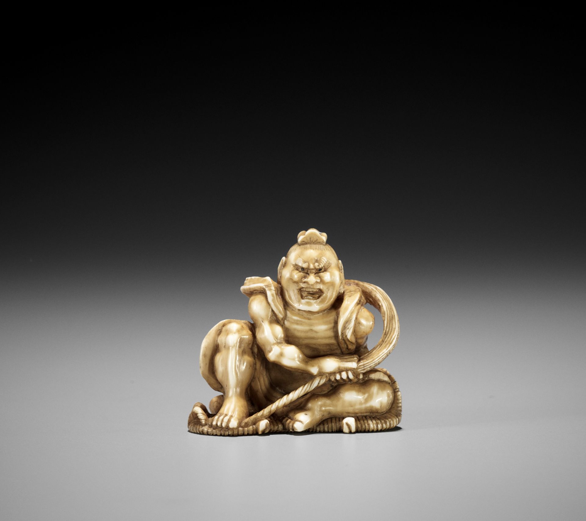 TOMOMASA: AN IVORY NETSUKE OF NIO BRAIDING A SANDAL