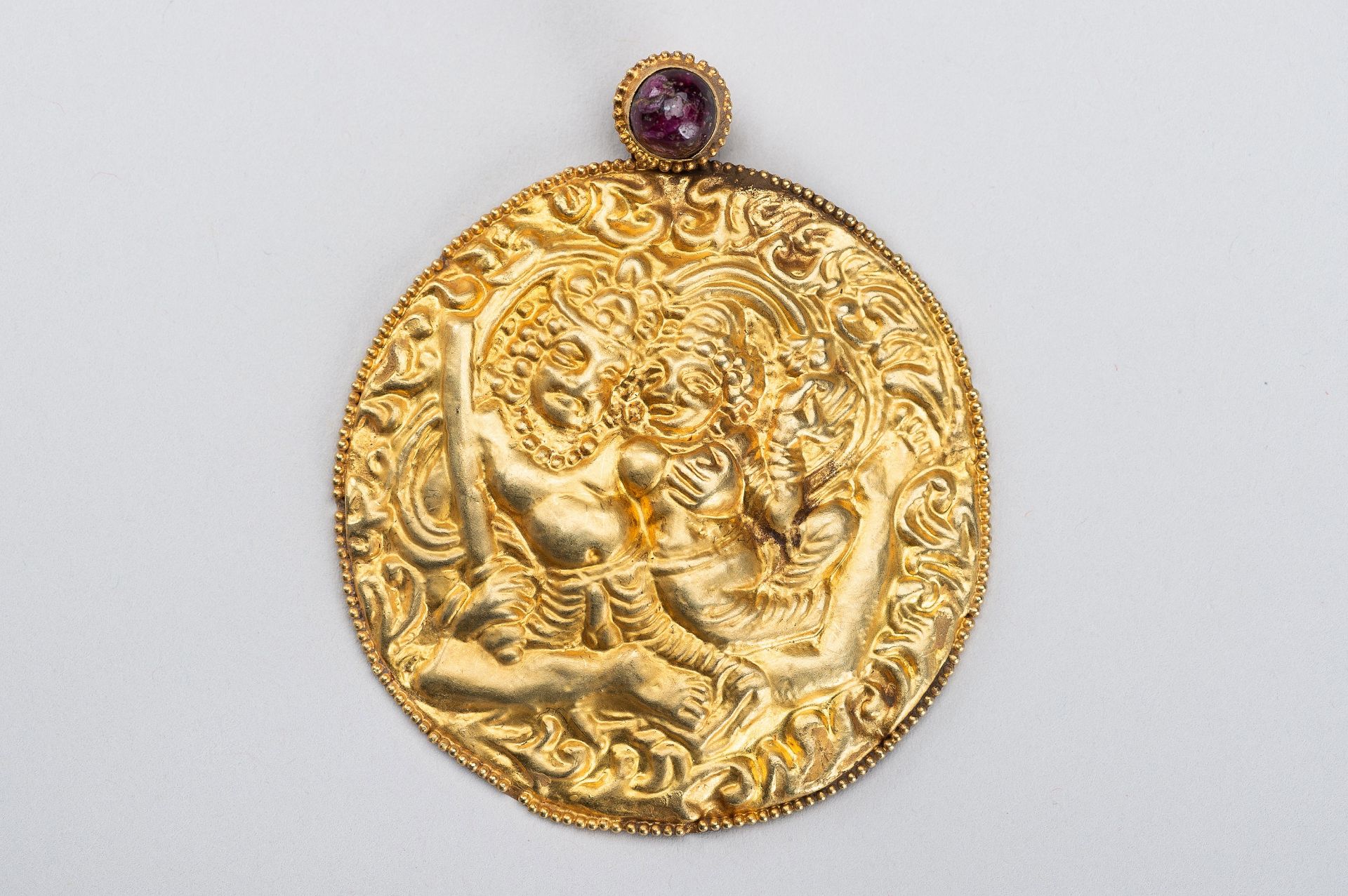 A GOLD REPOUSSE PENDANT WITH SHIVA AND PARVATI