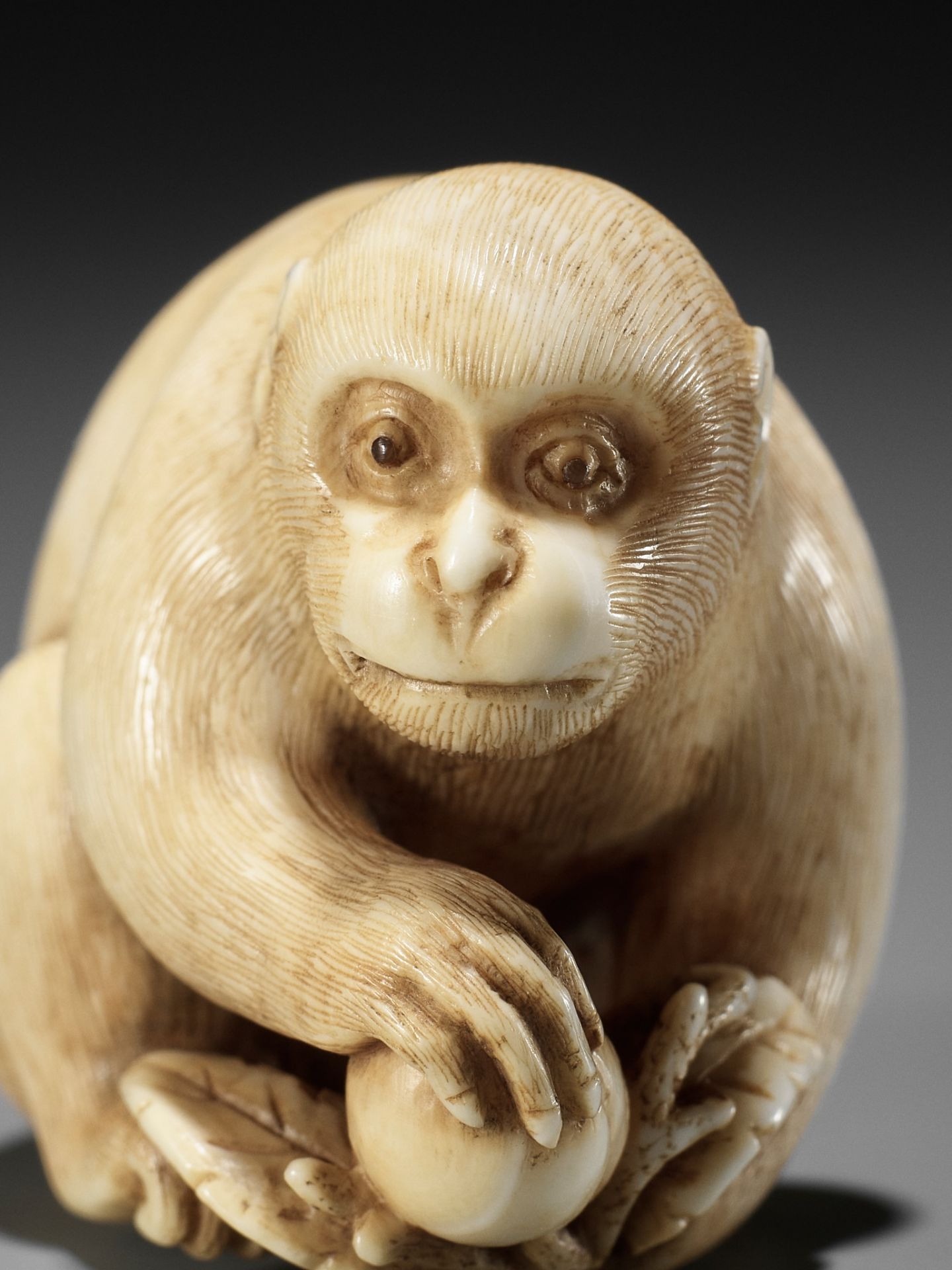 OKATORI: A FINE IVORY NETSUKE OF A MONKEY WITH A PEACH