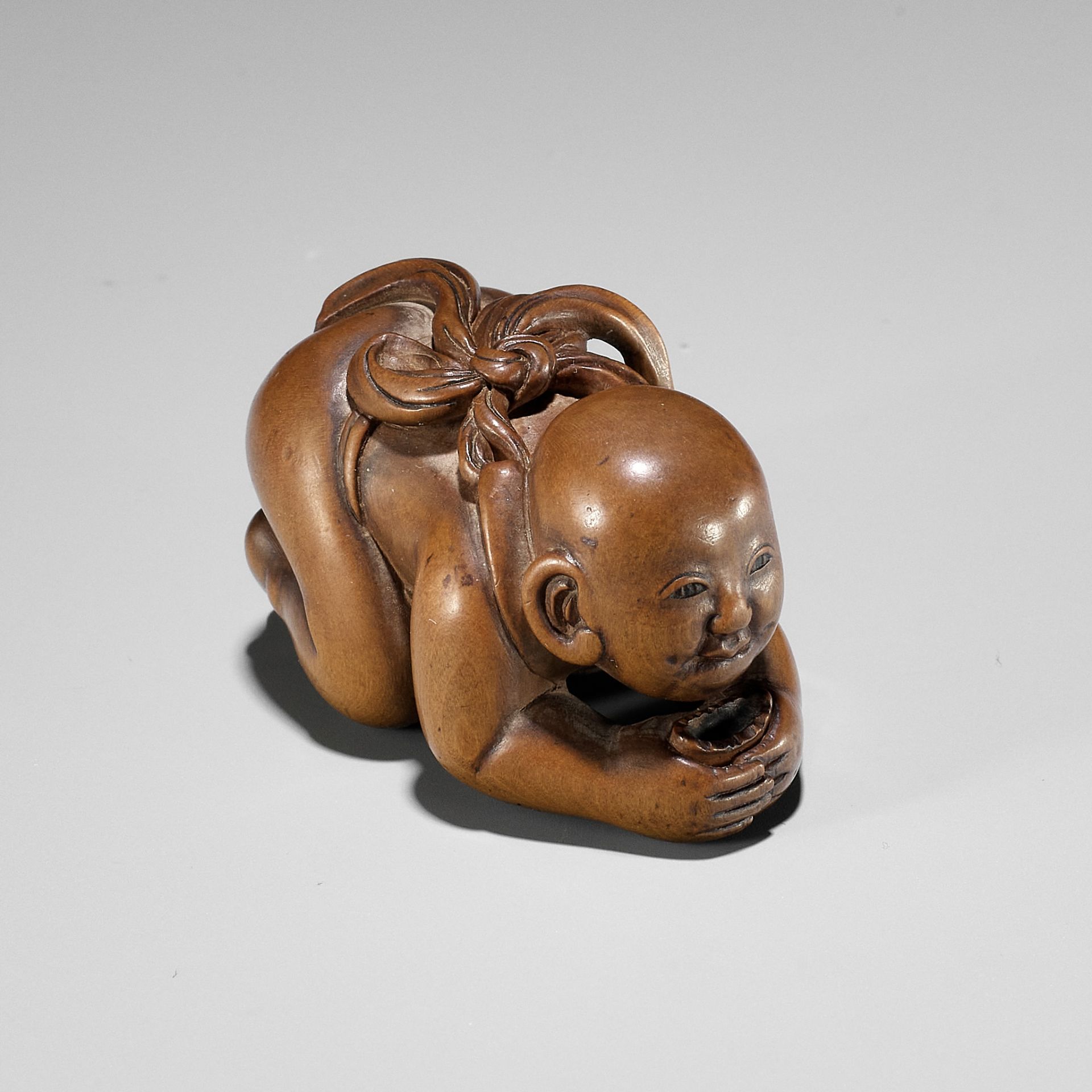 CHIKUUNSAI: A WOOD NETSUKE OF A BABY BOY EATING MOCHI