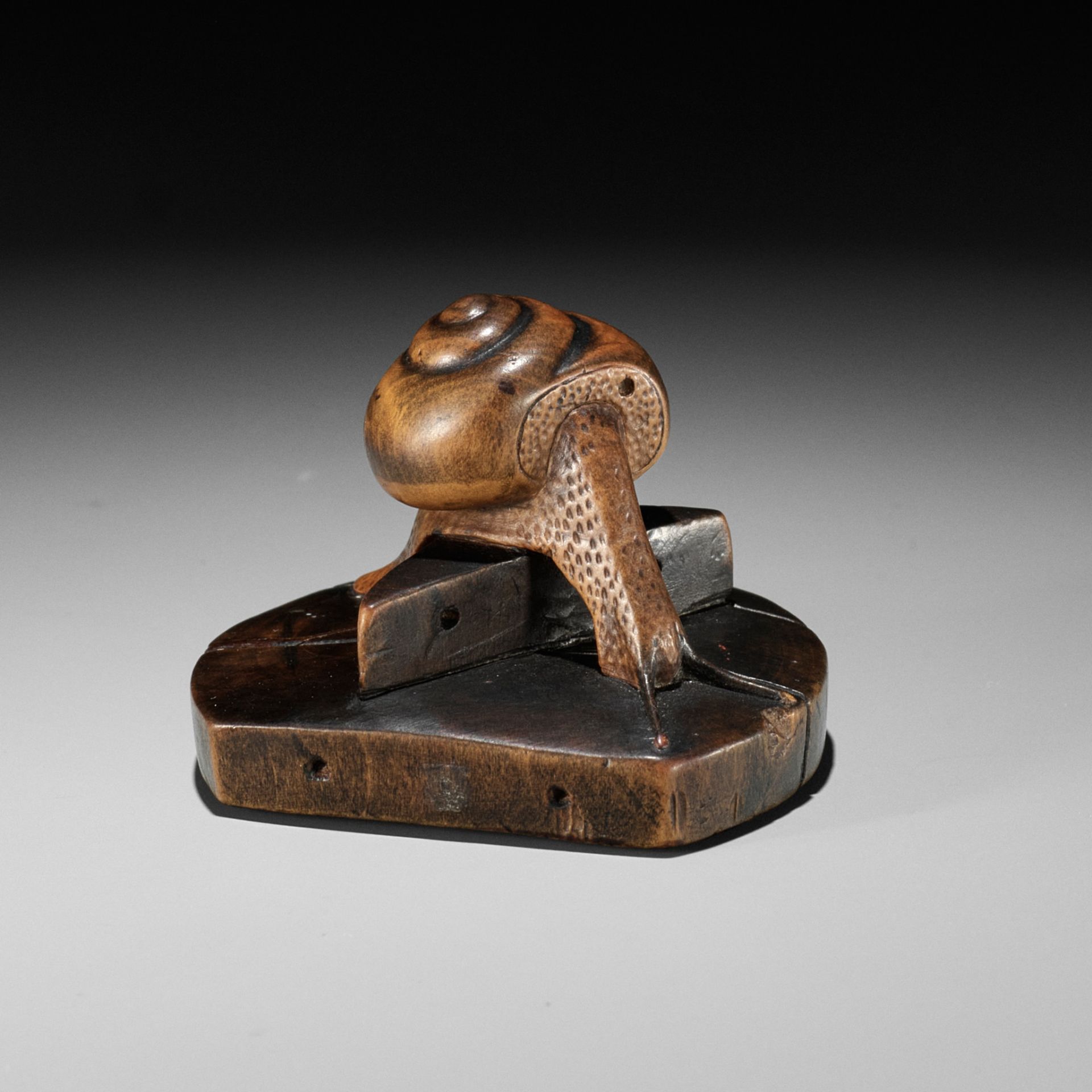 TOMOSHIGE: A RARE WOOD NETSUKE OF A SNAIL ON A WELL BUCKET COVER