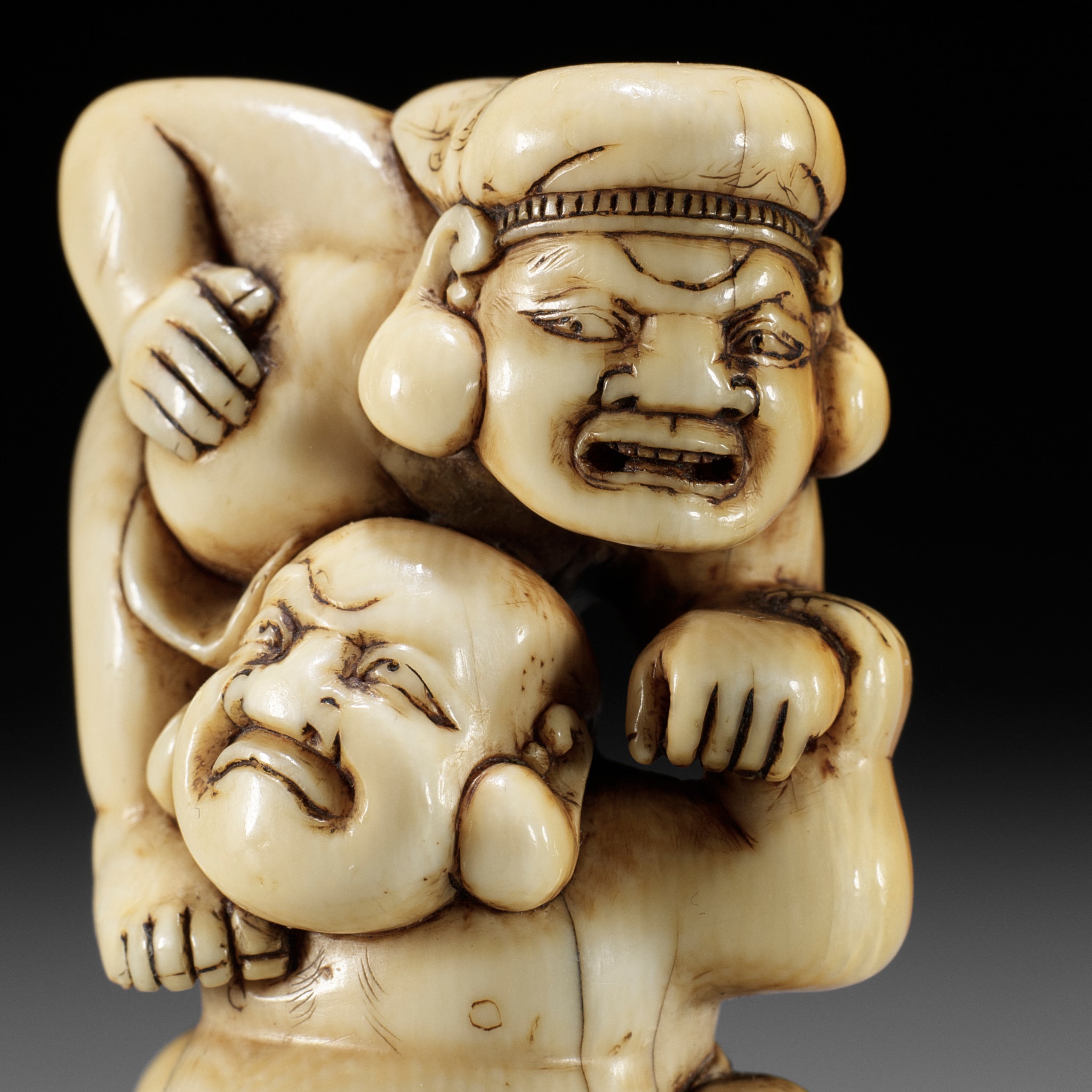 AN IVORY NETSUKE OF HOTEI AND DAIKOKU WRESTLING