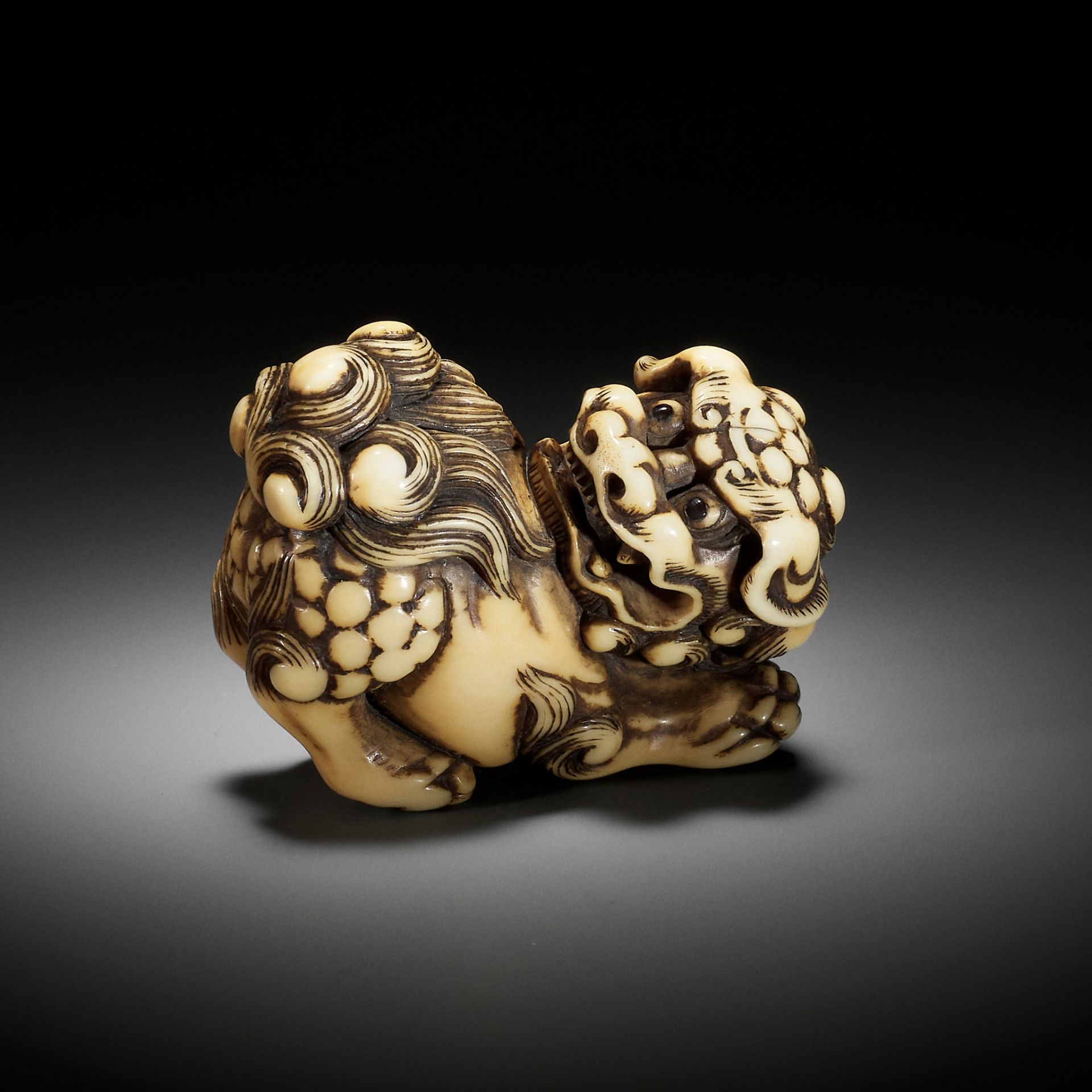 AN IVORY NETSUKE OF A PRANCING SHISHI