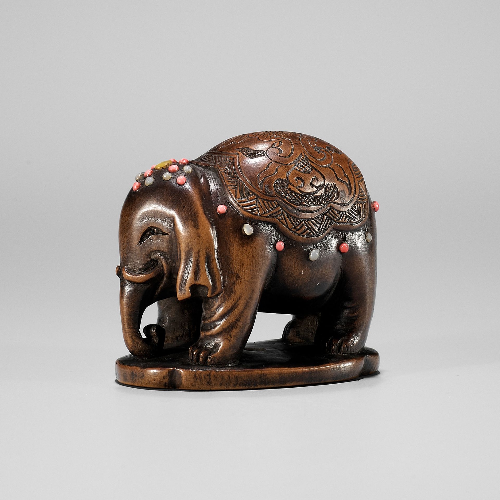 A RARE SHIBAYAMA-INLAID WOOD NETSUKE OF A CAPARISONED ELEPHANT