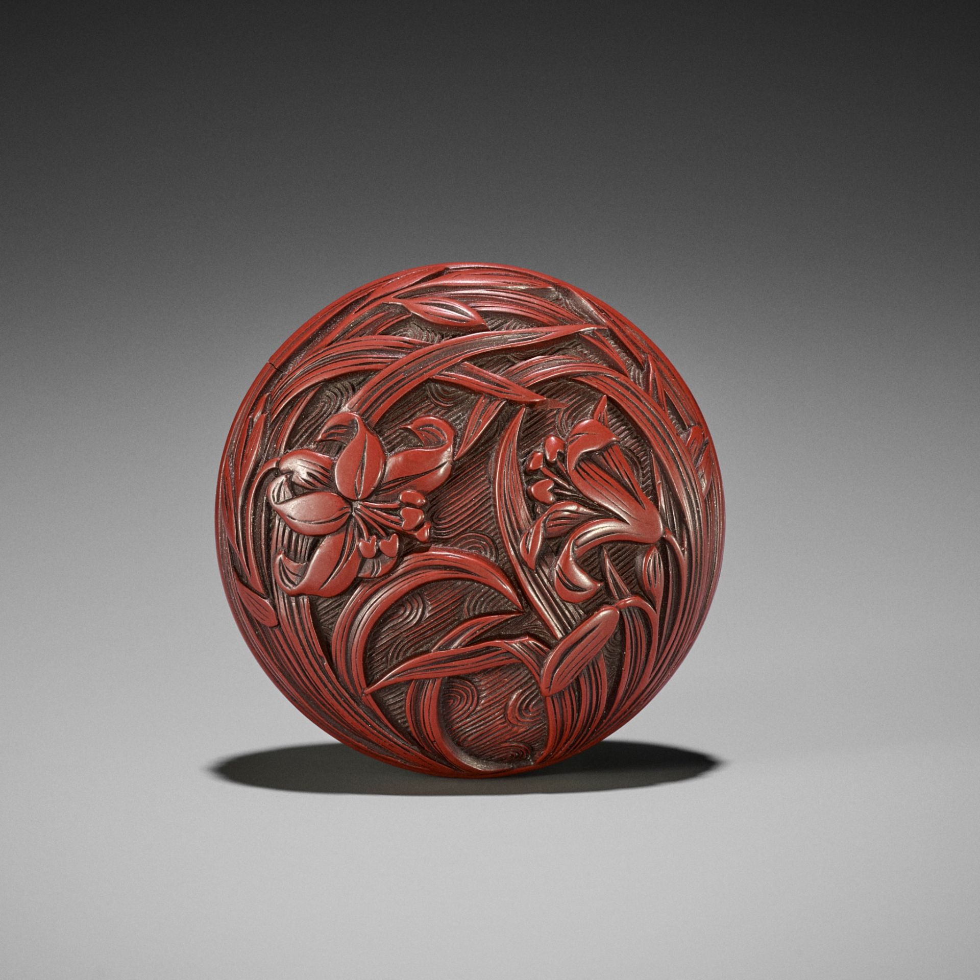 A FINE TSUISHU (CARVED RED LACQUER) MANJU NETSUKE WITH LILIES