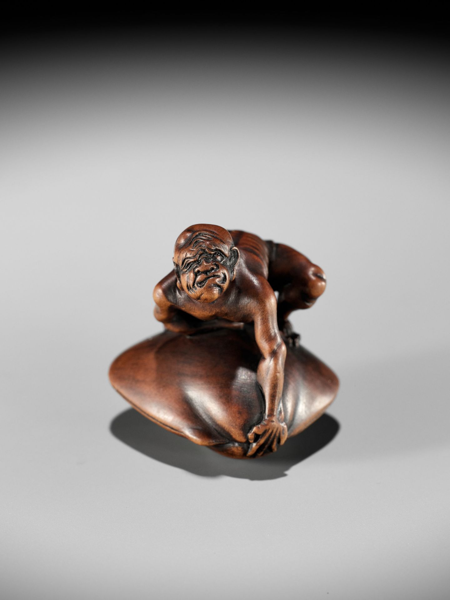 GYOKUZAN: A MASTERFUL MINIATURE WOOD NETSUKE OF A BLINDMAN BEING TRAPPED BY A CLAM