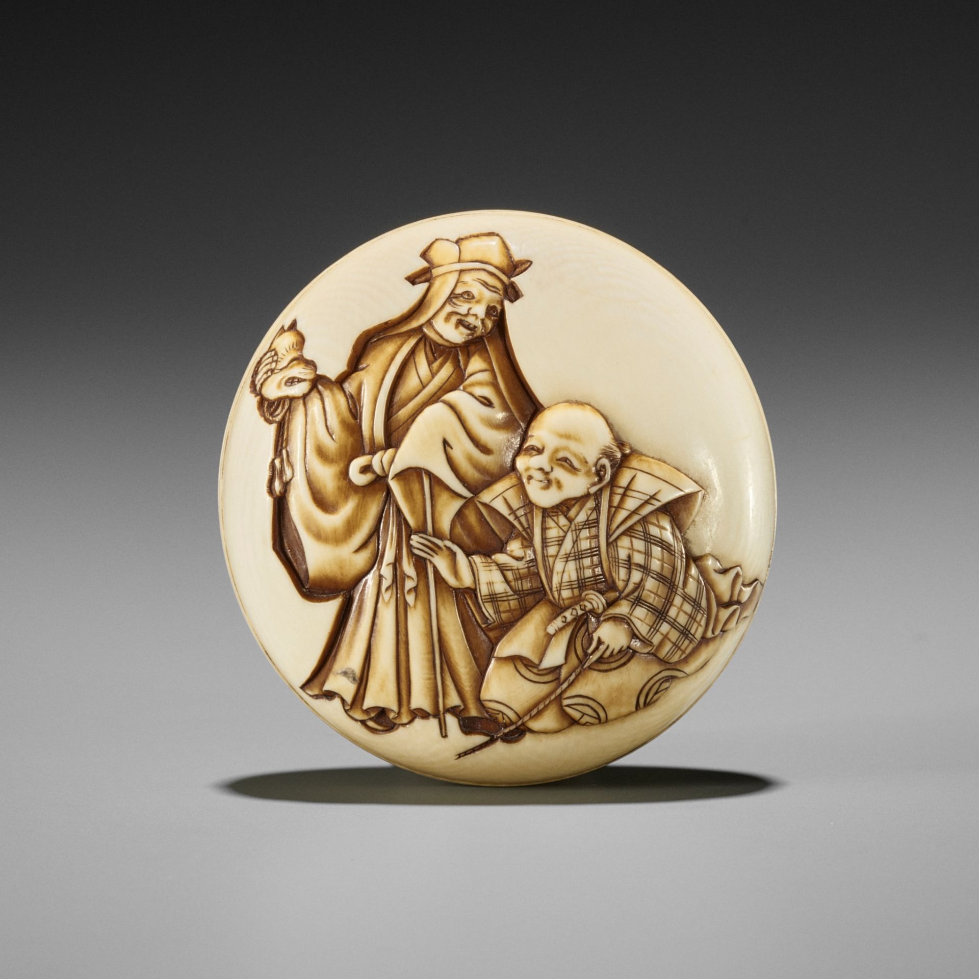 JUGYOKU: A FINE IVORY MANJU NETSUKE DEPICTING A SCENE FROM THE KYOGEN PLAY TSURIGITSUNE