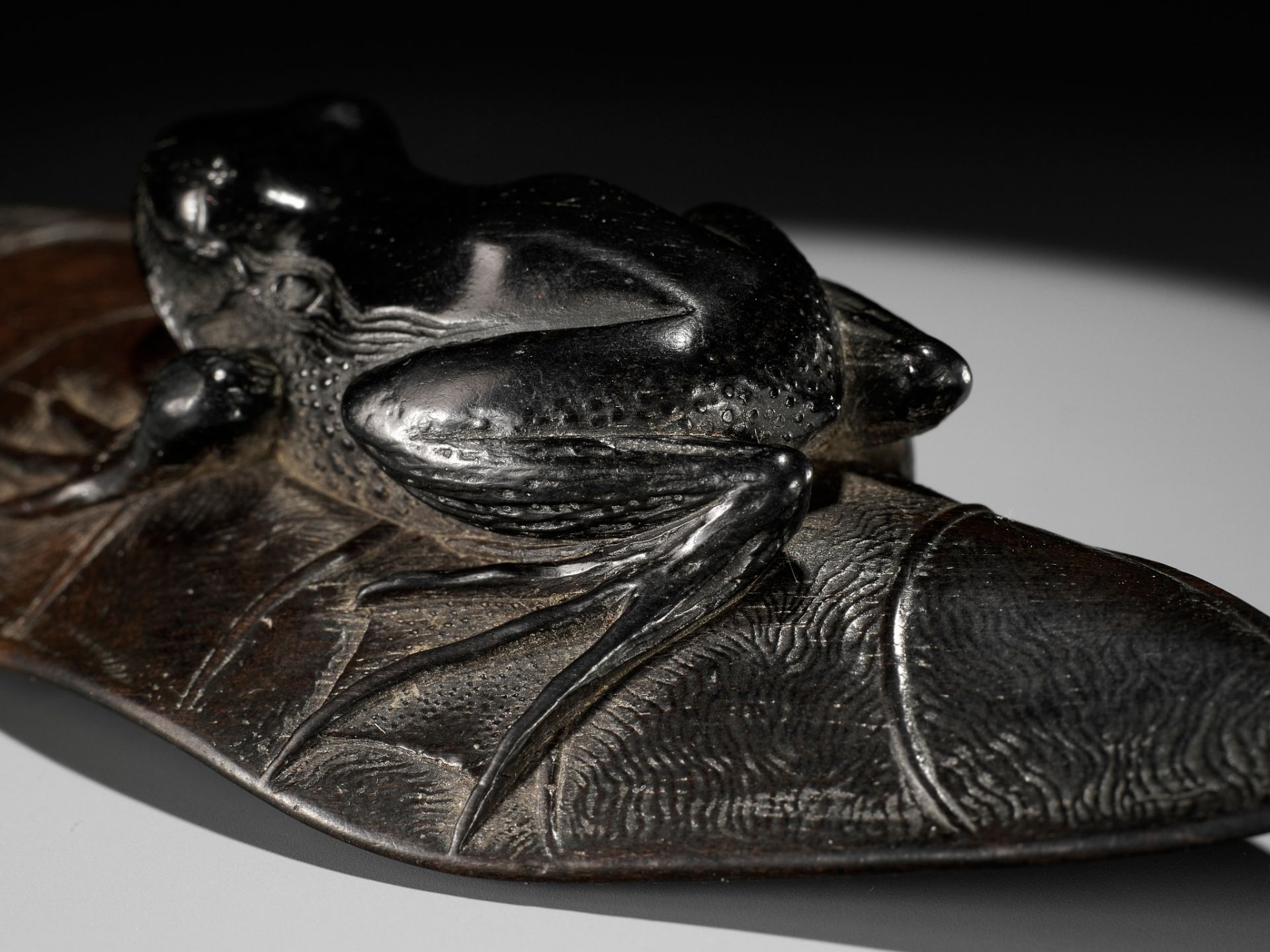 KANMAN: AN EXCEPTIONAL AND LARGE KUROGAKI (BLACK PERSIMMON) WOOD NETSUKE OF A FROG ON A LOTUS LEAF - Image 3 of 20