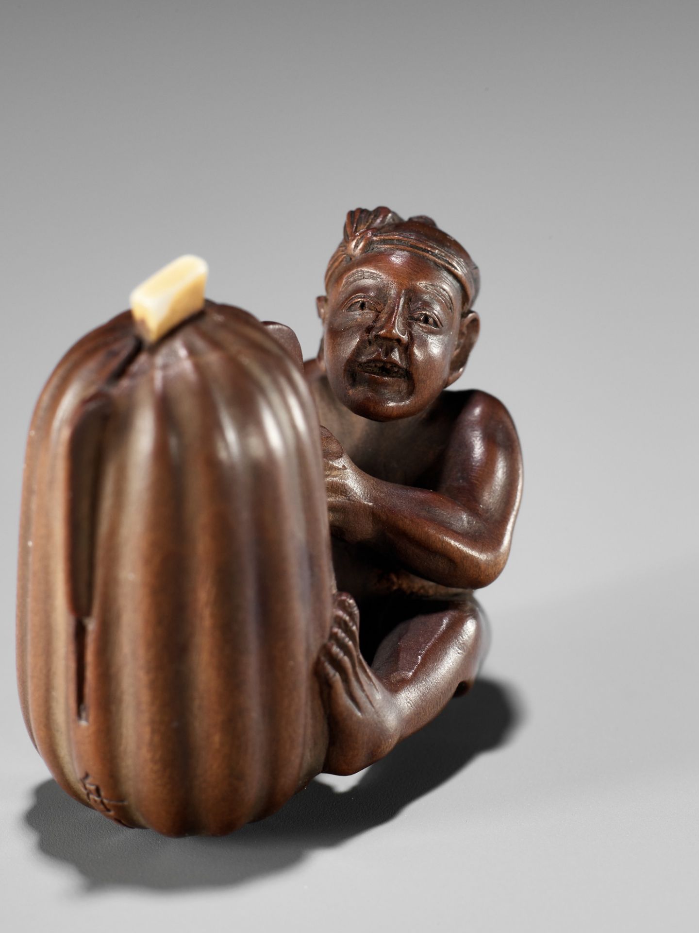 SHUGETSU SHIZAN: A FINE WOOD NETSUKE OF A MAN CUTTING A GIGANTIC GOURD