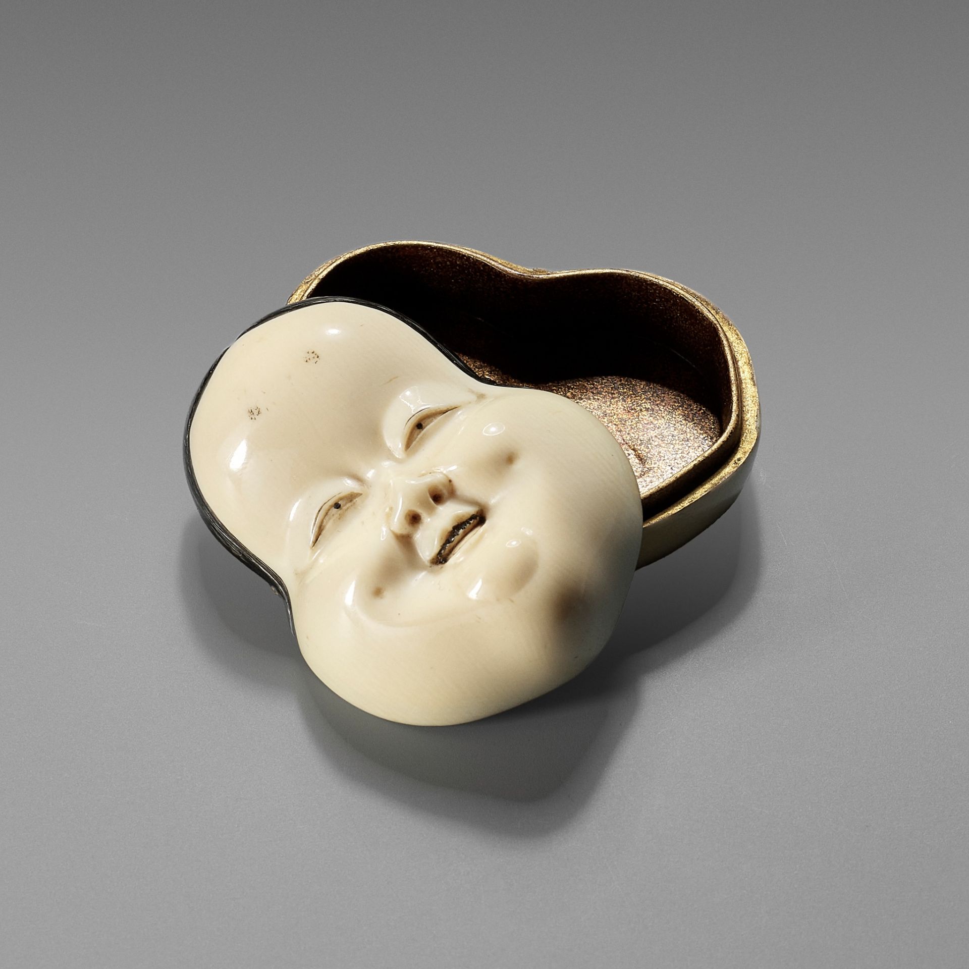YOZEI: A RARE LACQUERED IVORY HAKO (BOX) AND COVER IN THE FORM OF AN OKAME MASK, DATED 1705