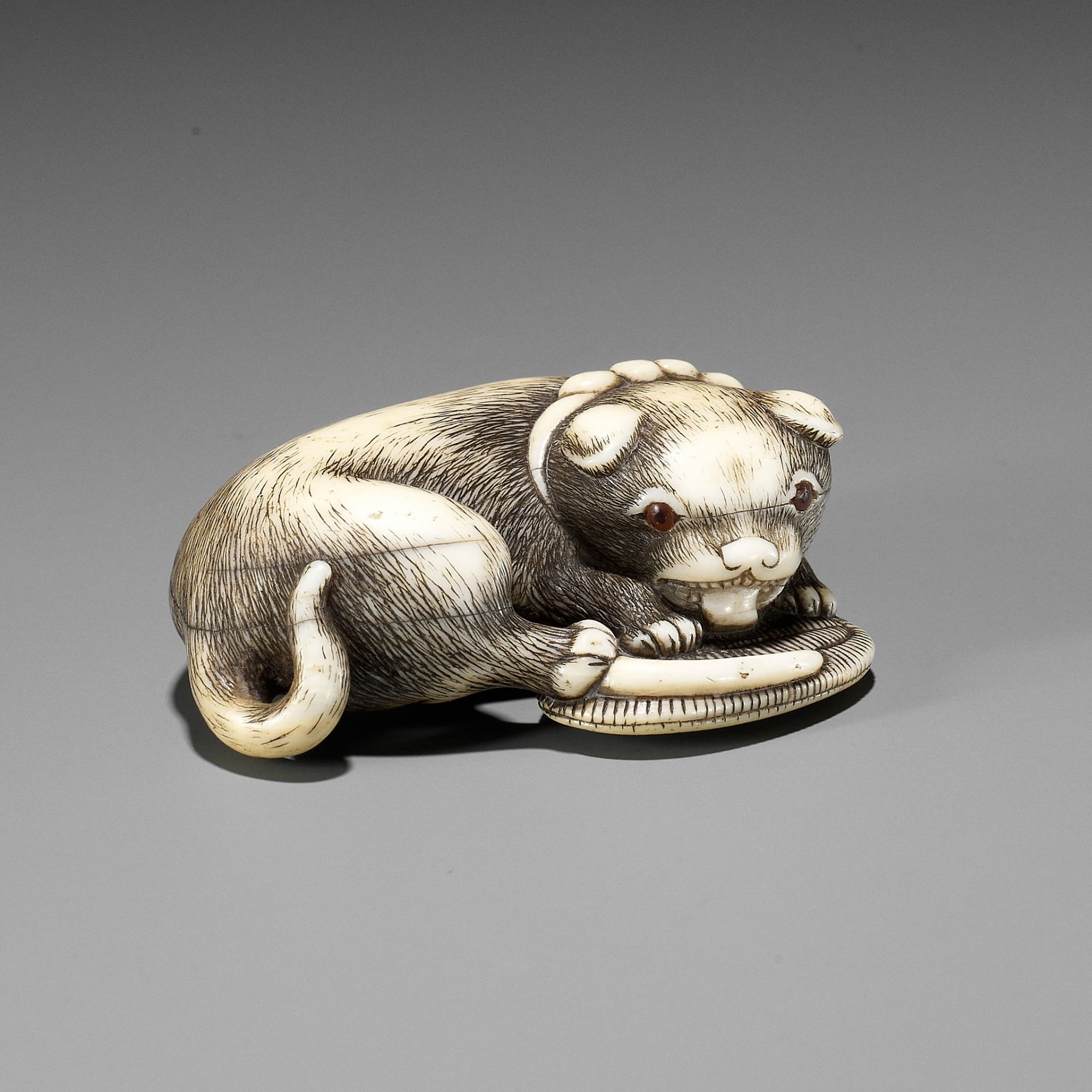 A FINE OSAKA SCHOOL IVORY NETSUKE OF A PUPPY PLAYING WITH A SANDAL (WARAJI)