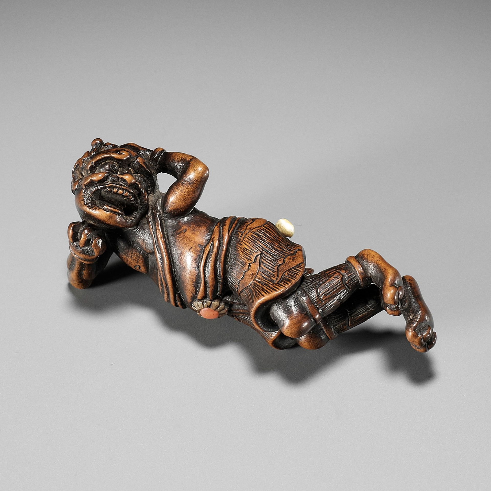 AN INLAID WOOD NETSUKE OF A RECLINING ONI AT SETSUBUN