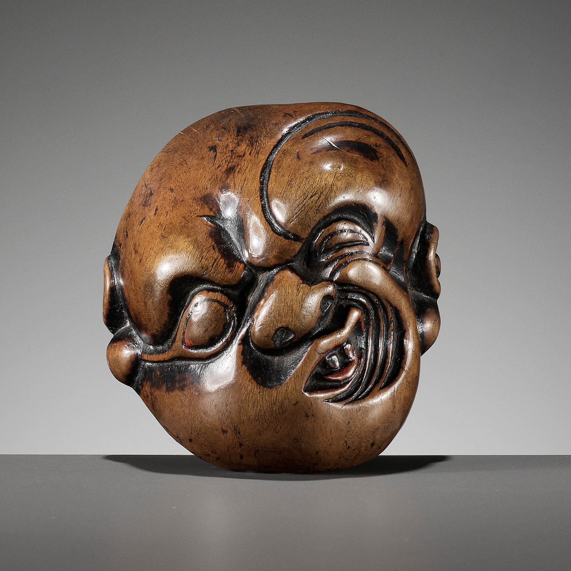 AN IMPORTANT EARLY WOOD MASK NETSUKE DEPICTING A GRIMACING MAN