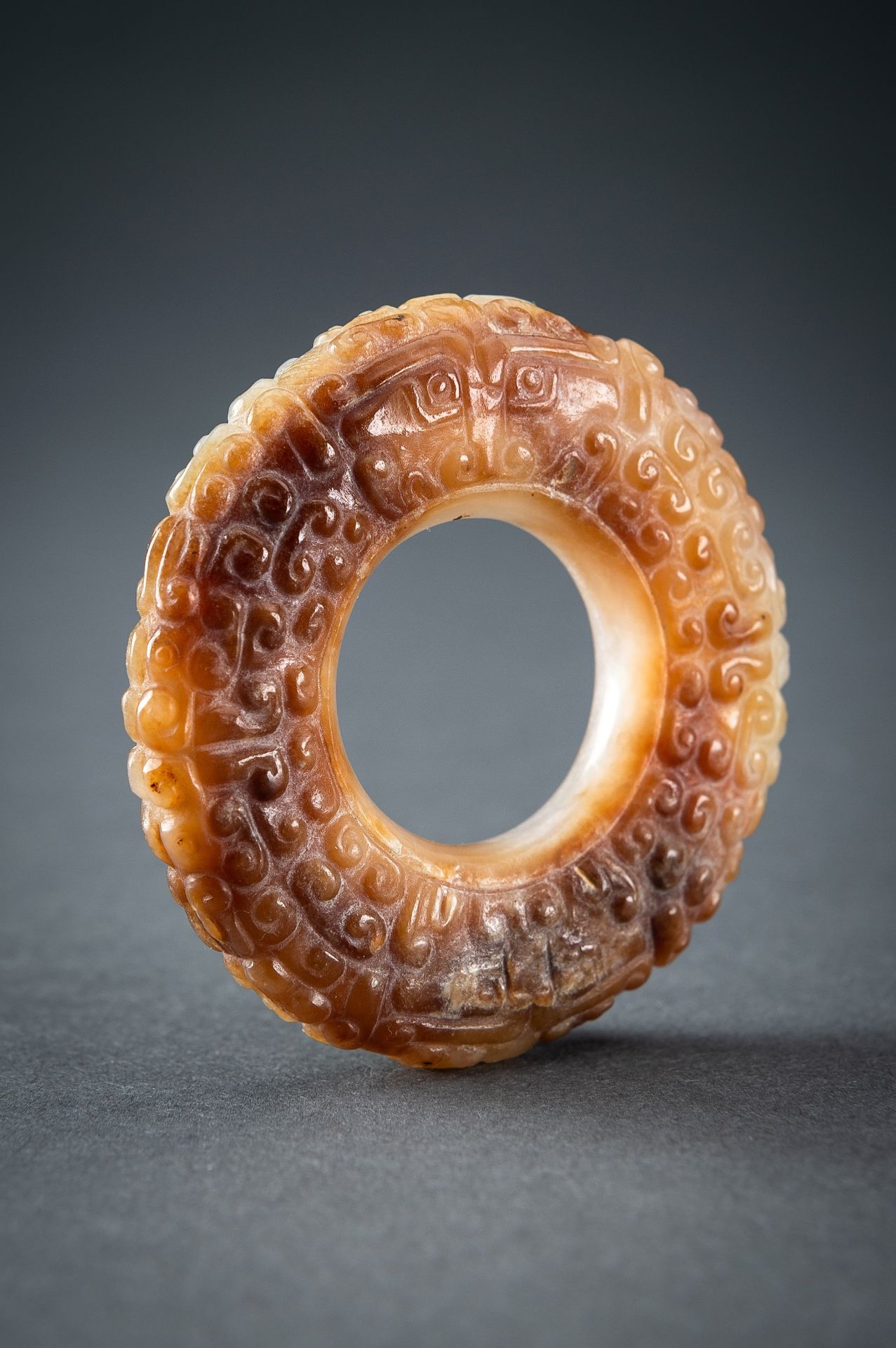 A WHITE AND RUSSET JADE 'CURLS AND TAOTIE MASKS' RING, HUAN, QING
