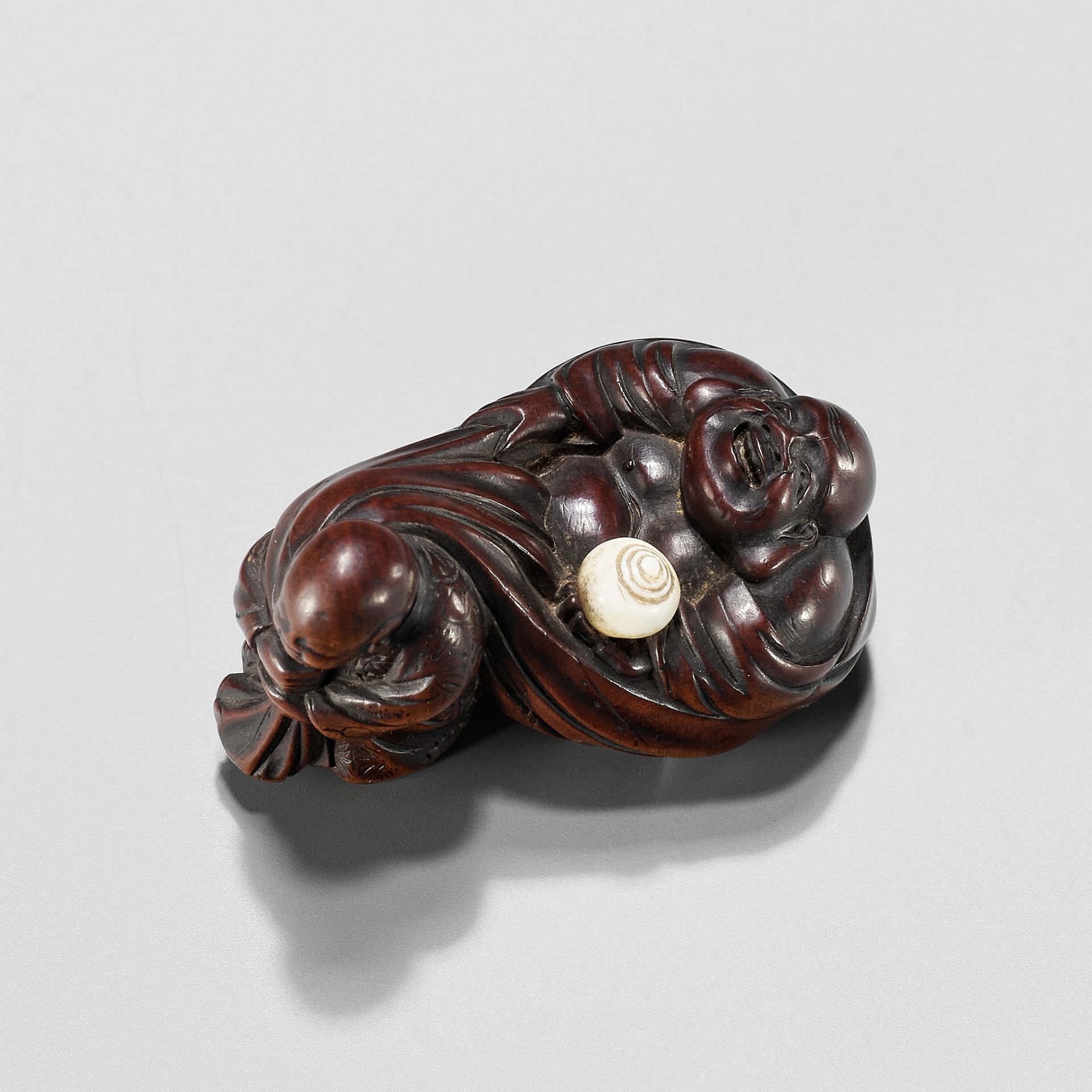 GYOKUMINSAI: A WOOD EDO SCHOOL NETSUKE OF A KARAKO PULLING HOTEI INSIDE HIS TREASURE BAG