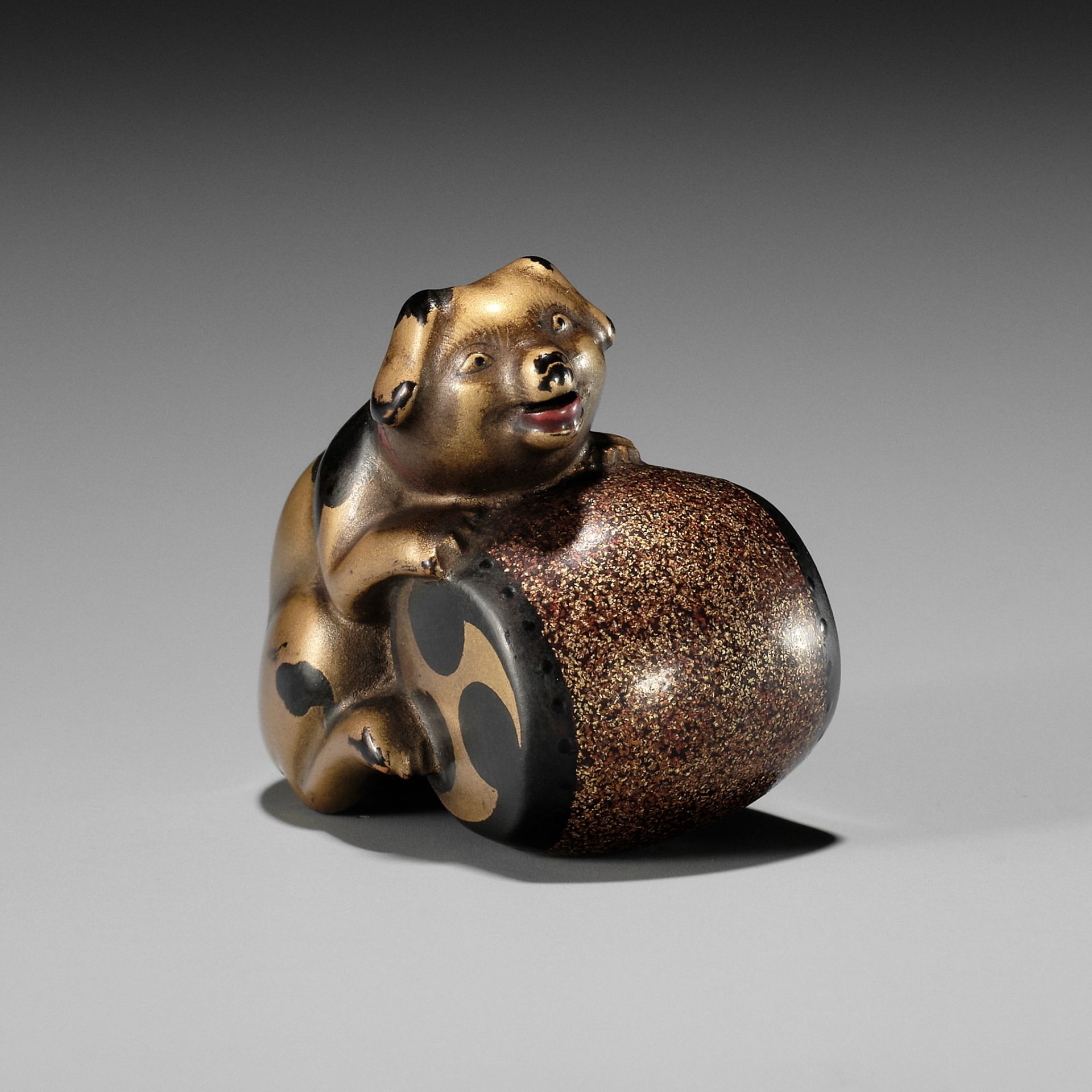 A CHARMING GOLD LACQUER NETSUKE OF A DOG WITH DRUM