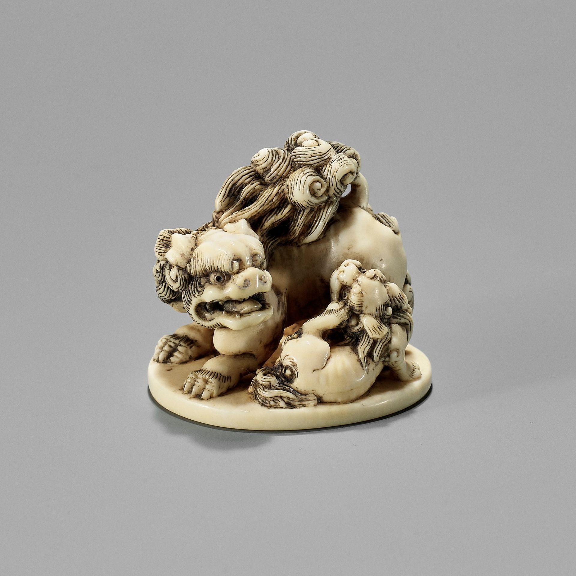 TOSHINAGA: AN IVORY NETSUKE OF A SHISHI WITH YOUNG