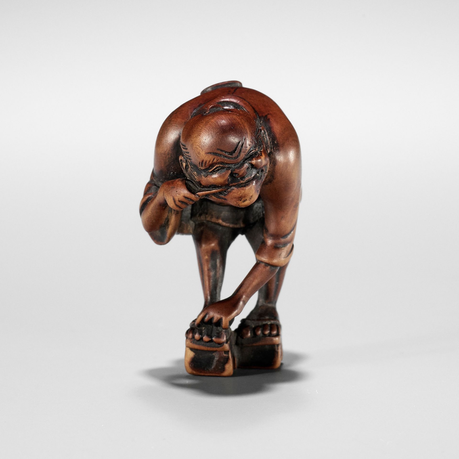 AN EDO SCHOOL WOOD NETSUKE OF A FARMER TYING HIS GETA AND CLEANING HIS TEETH