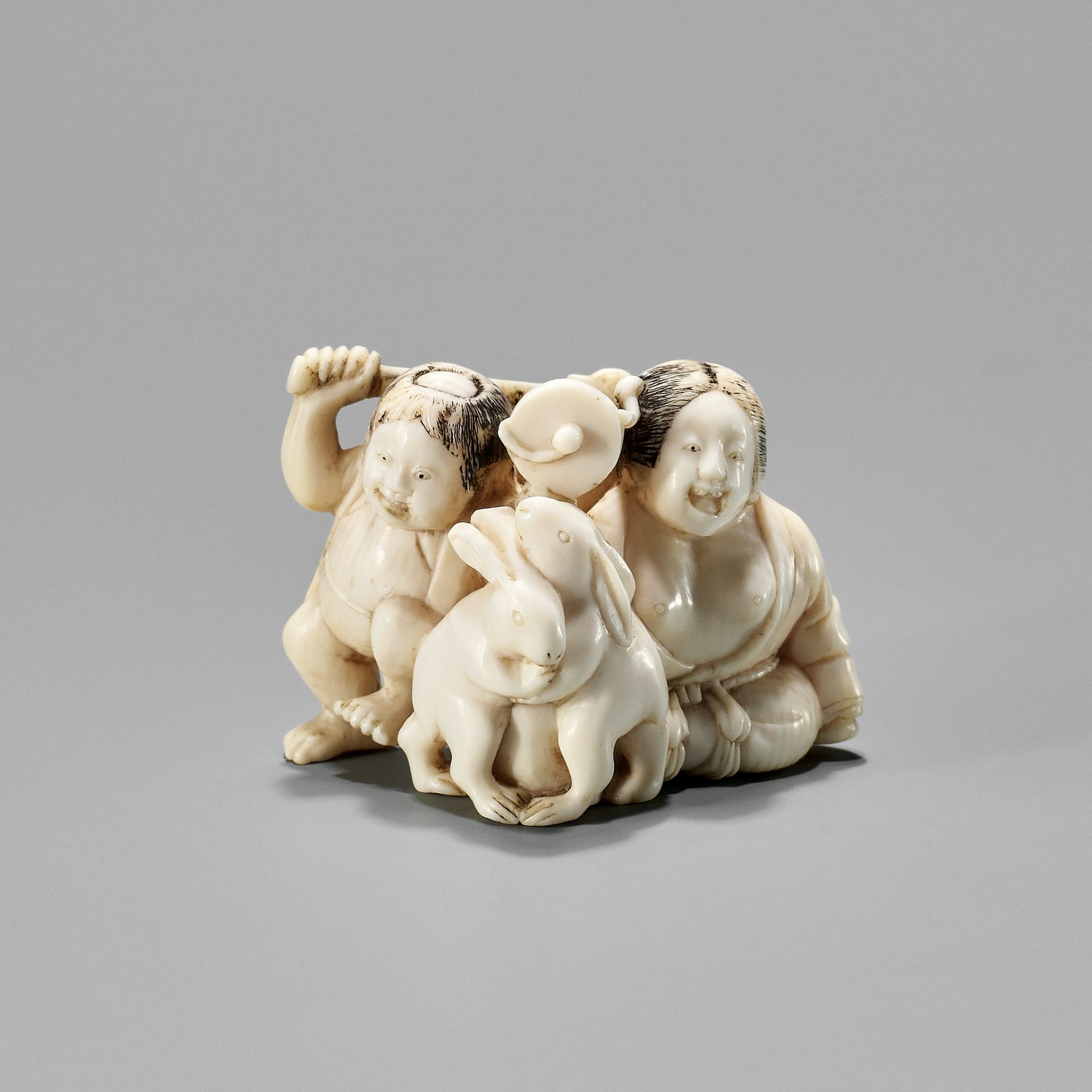 AN IVORY NETSUKE OF KINTARO AND YAMAUBA WATCHING TWO RABBITS WRESTLE