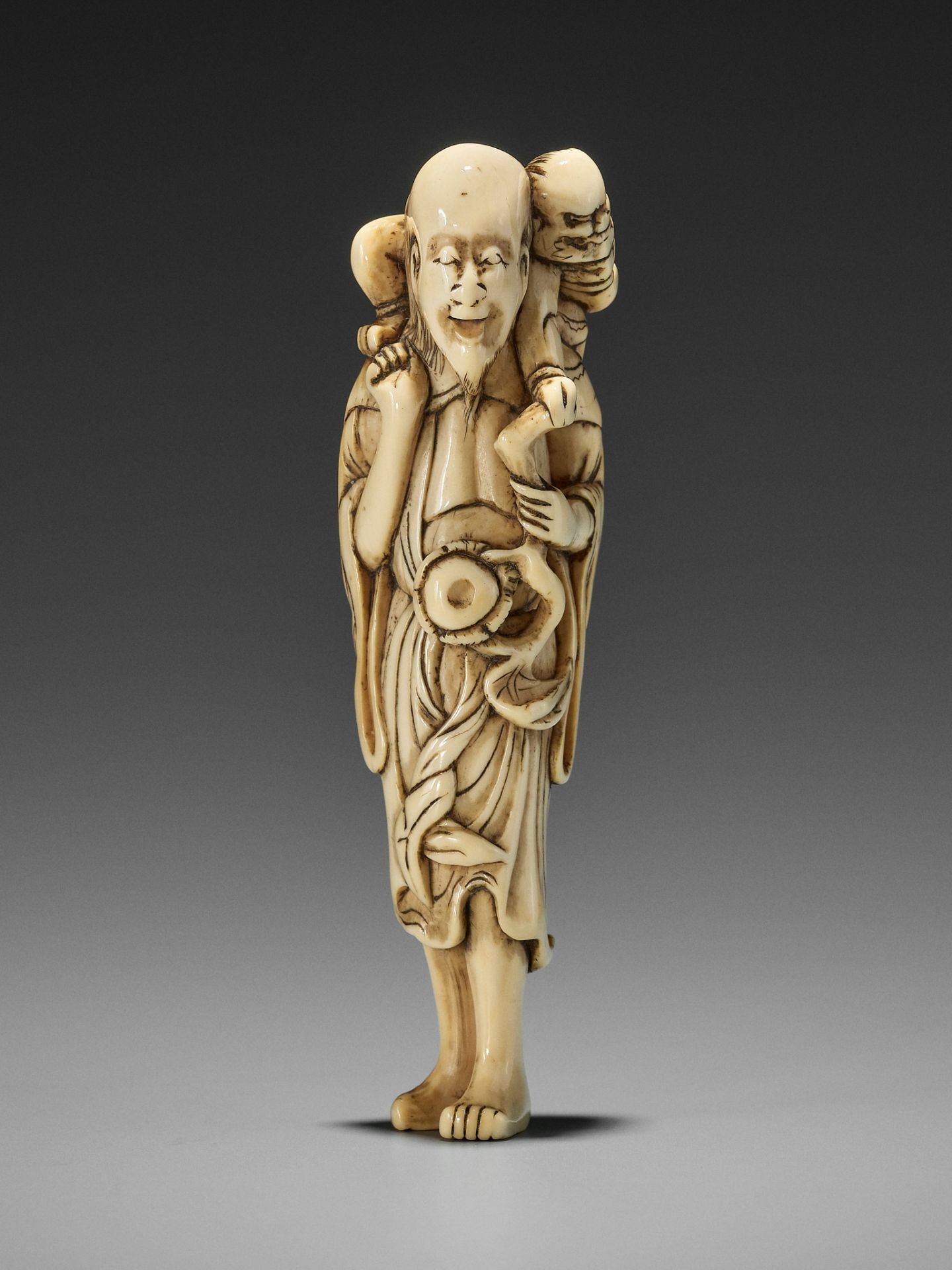 A RARE IVORY NETSUKE OF A SENNIN WITH ONI