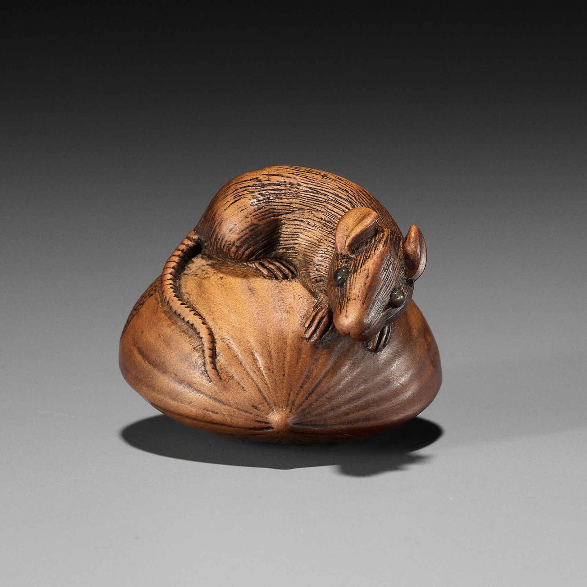 A WOOD NETSUKE OF A RAT ON A HUGE CHESTNUT