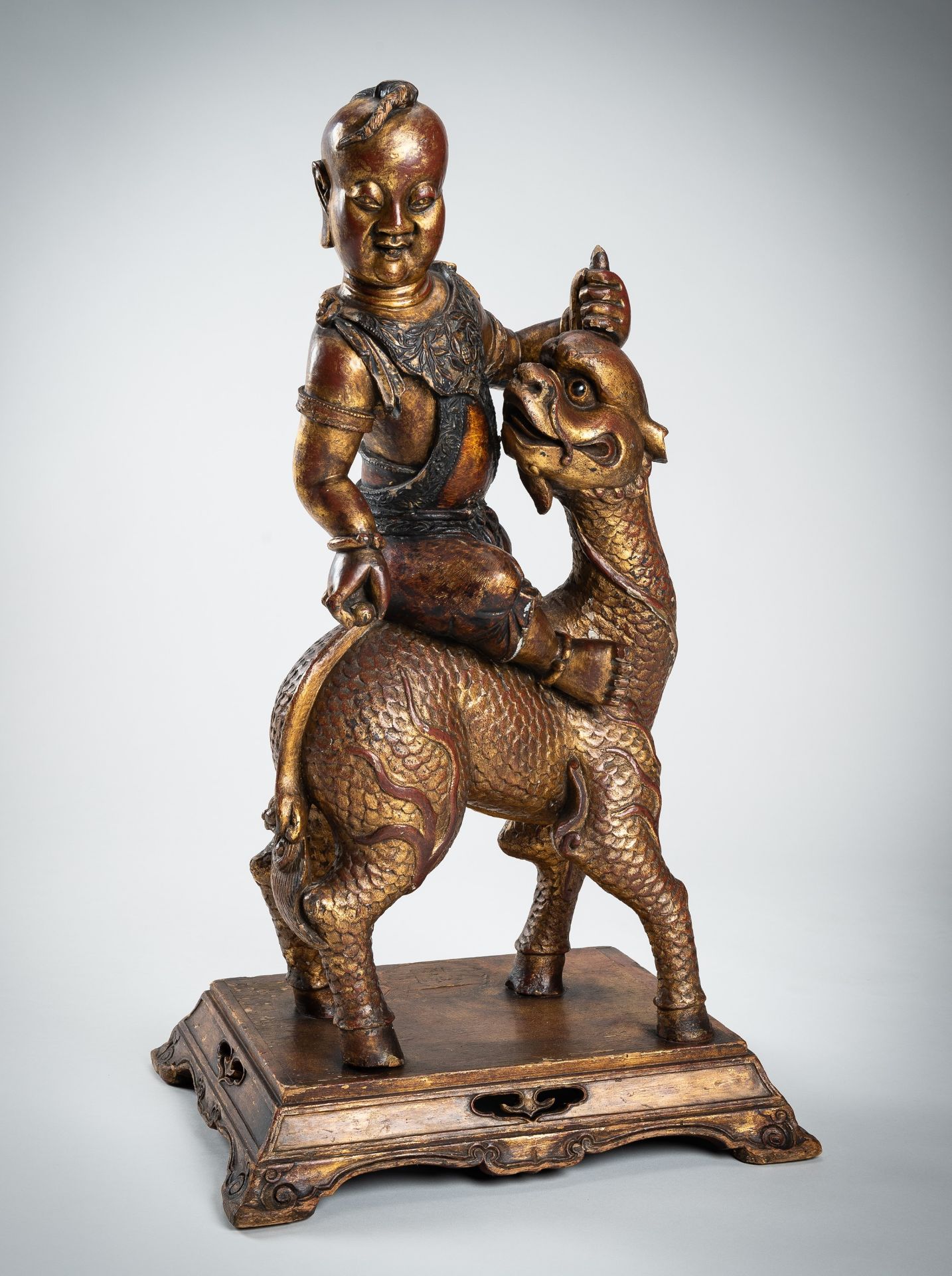 A VERY LARGE GILT-LACQUERED WOOD STATUE OF YOUNG BUDDHA RIDING QILIN