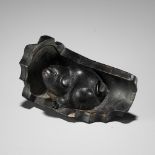 A RARE HORN NETSUKE OF A PUPPY NESTLED WITHIN A ROOF TILE, ATTRIBUTED TO HORAKU