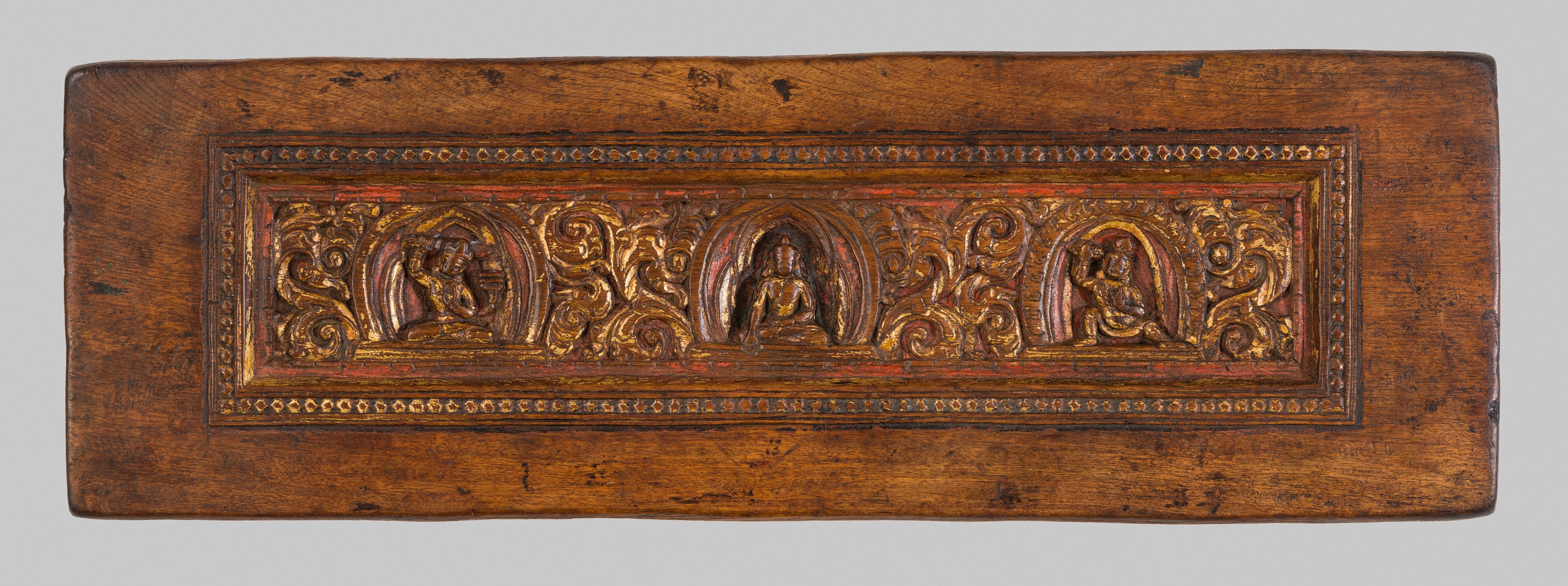 A GILT AND PAINTED WOOD MANUSCRIPT COVER DEPICTING A BUDDHIST TRIAD, TIBET, 12TH-13TH CENTURY