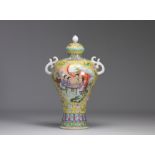 Covered porcelain vase decorated with characters from the Famille Rose on a yellow background