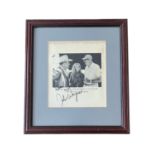 John Wayne (1907-1979) – A framed black and white photograph signed by John Wayne in black ink “Good
