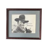 John Wayne (1907-1979) – A framed black and white photograph signed by John Wayne in black ink “Good