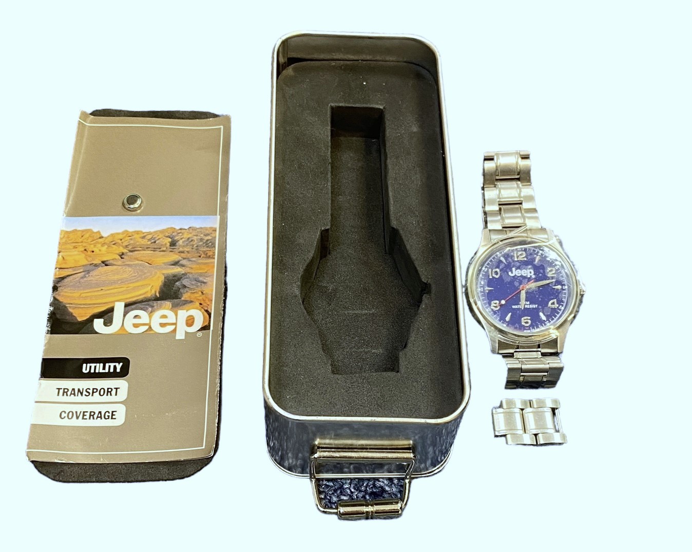 A Jeep blue faced water resistant wristwatch with stainless steel strap. (2006). In Jeep metal tin