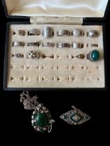 A case containing a number of silver rings . Also a 925 green gem set brooch and a white metal green