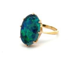 A solid black opal ring set in 18ct yellow gold, showing good blue and green play of colour. Opal