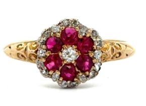 A ruby and diamond flower ring with scroll shoulders, stamped 18ct, size P. 3.02g. Please see the