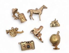 A range of seven charms, five fully hallmarked 9ct gold, two (globe and cannon unmarked). Also