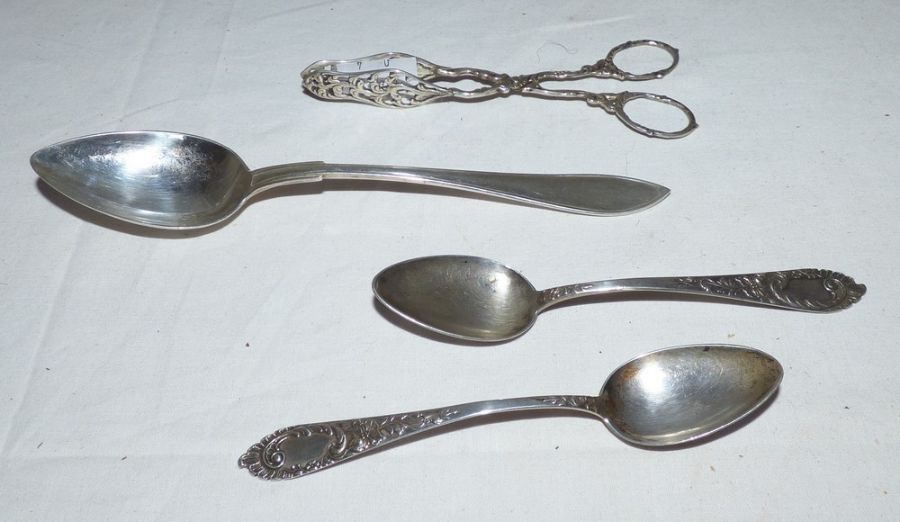 A pair of white metal cast and foliate pierced tongs, a pair of German silver teaspoons with