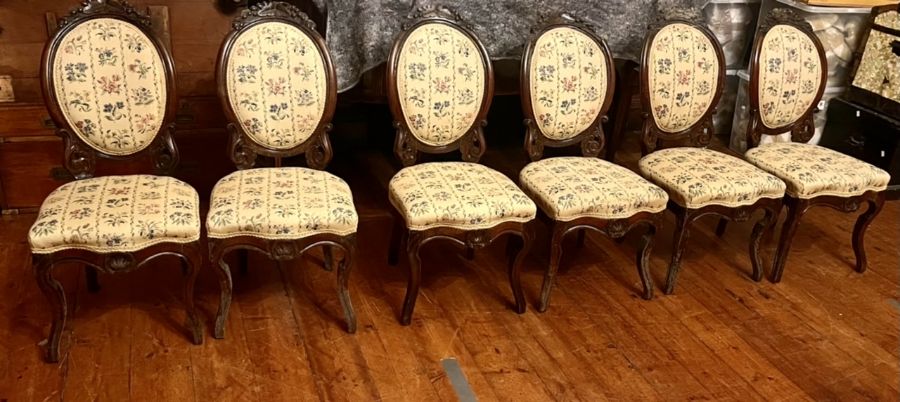 A set of six Victorian upholstered walnut dining chairs, the oval backs surmounted by carved