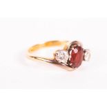 A garnet and diamond set trilogy ring, set in a yellow metal bypass mount. The garnet, an oval mixed