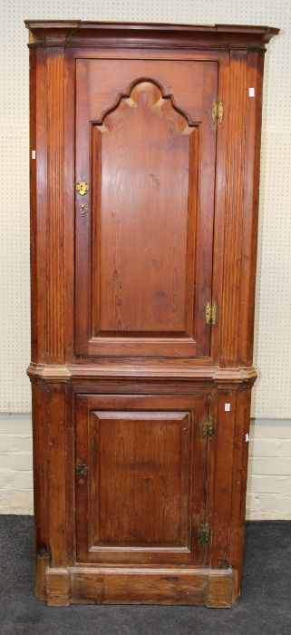 An early 19th century pitched pine floorstanding corner cupboard, the inverted breakfront cornice