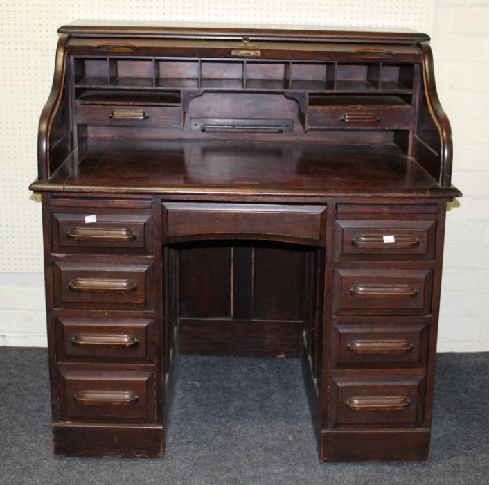 An early 20th century oak roll top desk, the fall enclosing a fitted interior raised on a pair of