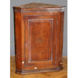 An early 19th century oak wall mounting corner cupboard, the moulded cornice over parquetry star